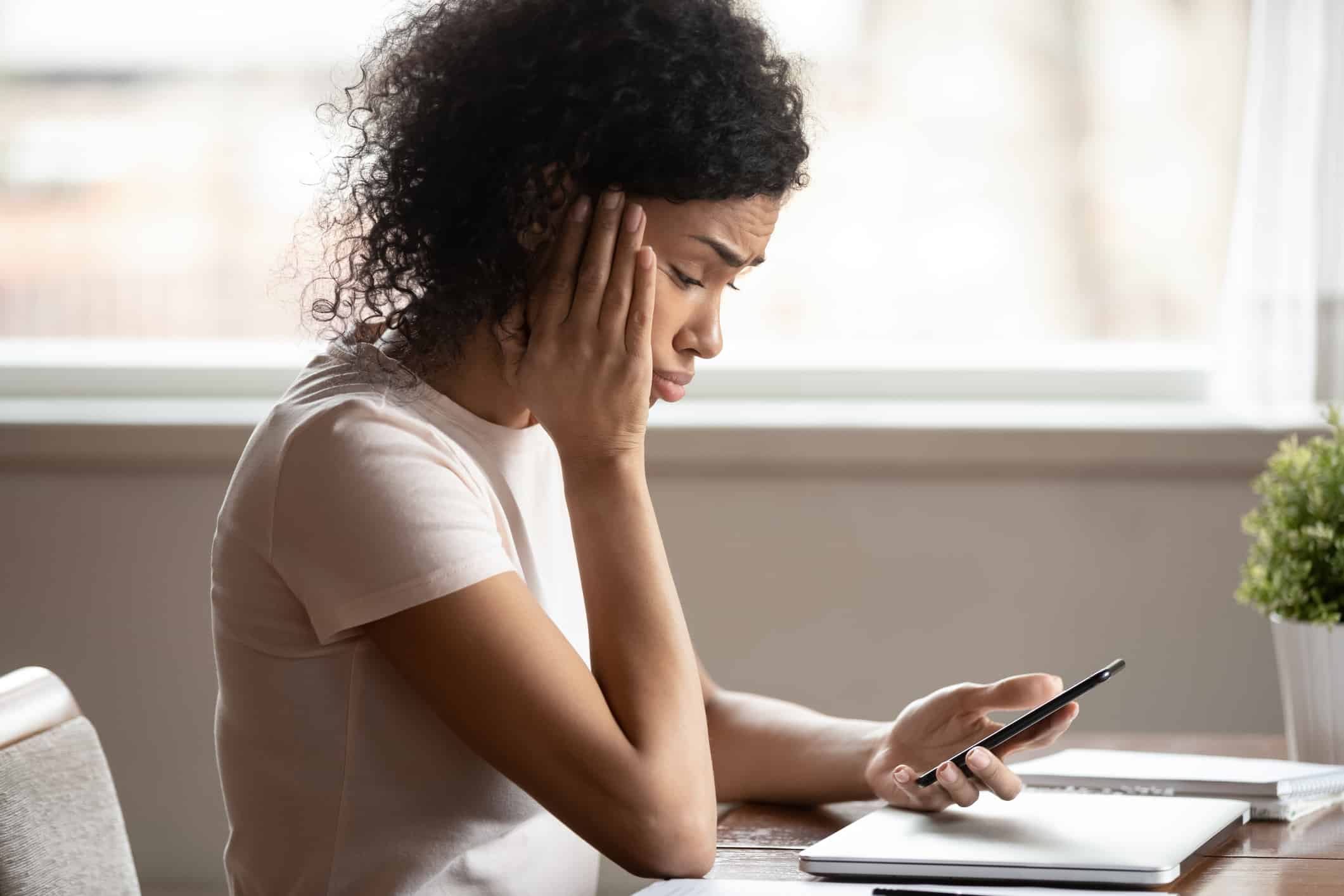 African woman looking at mobile phone screen feels upset
