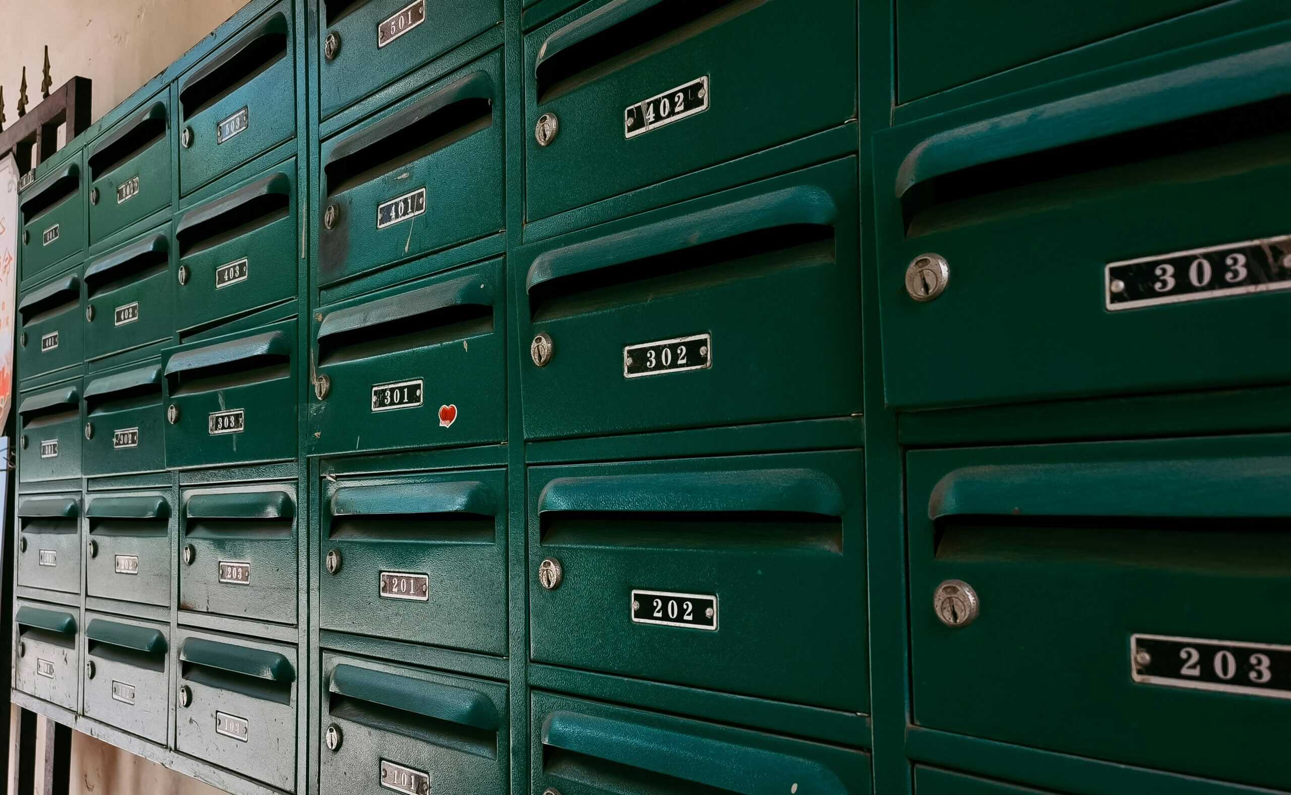 A wall of rows of green mailboxes with numbers, key holes, and mail slots